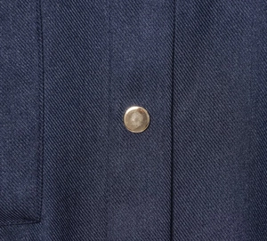 Gros plan sur le tissu sergé bleu marine avec un bouton en métal doré rond et poli