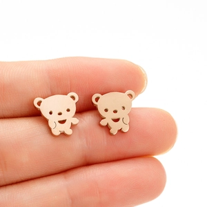 Close-up of small rose gold bear stud earrings held on fingertips for scale