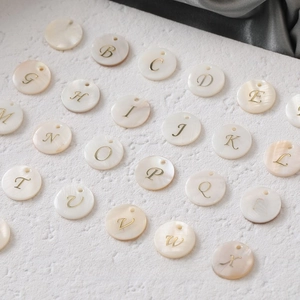 Macro view of natural freshwater shell round pendants with gold letter engravings