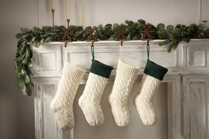 Macro detail of cable knit Christmas stockings with pine branches on a fireplace