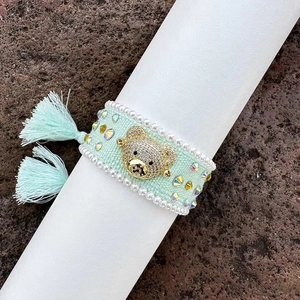 Macro view of hand-woven mint green bracelet with crystal bear charm and pearl trim