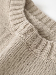 Close-up detail of the ribbed crew neck and soft oat beige knit texture of the sweater