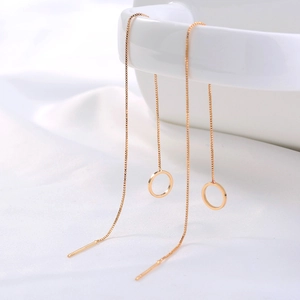 Elegant gold drop earrings with sleek circle charms hanging on a white ceramic vase