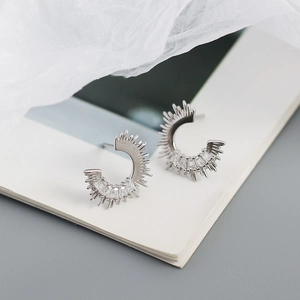 Macro detail of S925 silver C-shape earrings with zircon studs on a book page