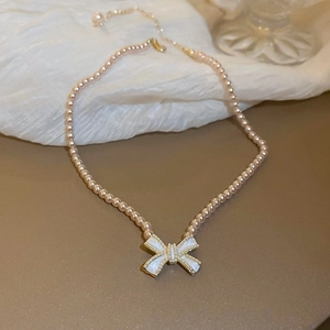 Detail einer rosa Perlenkette mit weißem Emaille-Schleifenanhänger und Goldakzenten