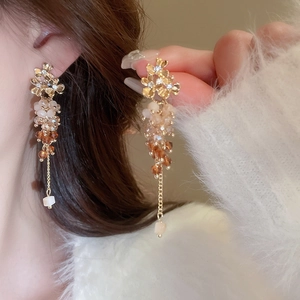 Close-up of elegant gold flower beaded tassel earrings worn by a model in soft lighting