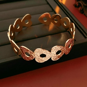 Detailed close-up of golden hollow heart bangle with intricate floral embossed patterns