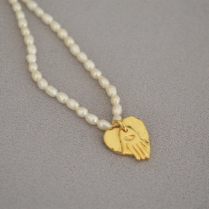 Detail of freshwater pearl necklace with gold heart charm and embossed eye pattern