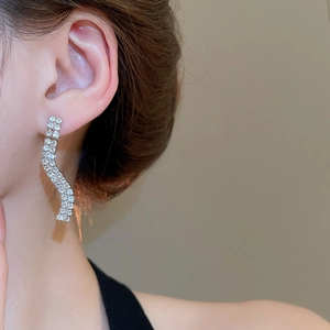 Close-up of elegant silver wave-shaped earrings with rhinestones worn by a model