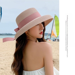 Detail view of khaki straw sun hat with pink ribbon bow on a scenic beach background