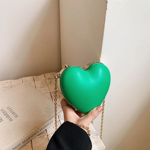Mini bright green heart shaped crossbody bag with gold chain strap held by a model