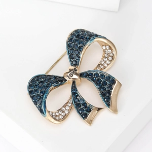 Detail of a gold bow brooch featuring blue crystals and a heart engraved with love