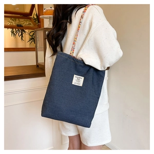Détail du cabas en denim bleu avec bandoulière tissée porté à l'épaule du mannequin