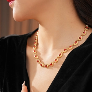 Gros plan d'un collier vintage doré avec gemmes rouges ovales sur un haut noir à col en V