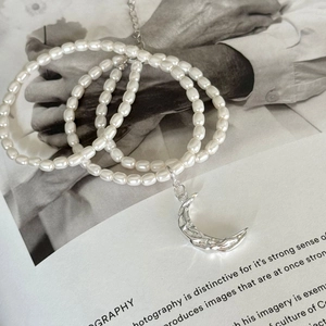 Detailed close-up of 925 silver crescent moon pendant and pearls on art magazine