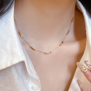 Close-up of a delicate gold stainless steel necklace with small square beads on a model