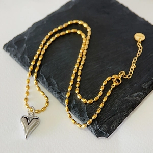 Détail du pendentif cœur bicolore sur chaîne à billes dorées sur fond de pierre noire