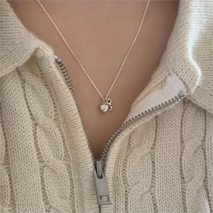 Close-up of a silver heart and key pendant necklace worn on a cream knit sweater