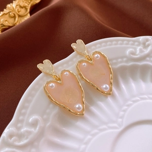 Detail of gold-plated heart drop earrings with pink resin and white pearls on a white plate