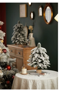Miniature flocked PE Christmas tree with snow effect and natural wooden base on a white table