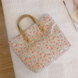 Detail of floral canvas tote bag showing faux leather handles and gold rivet accents