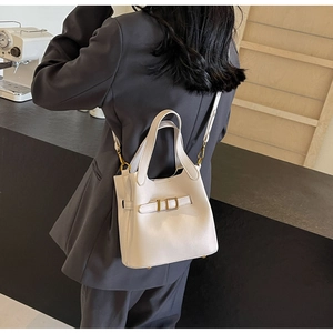 Detail of a cream lychee grain leather bucket bag with golden metal buckle and straps