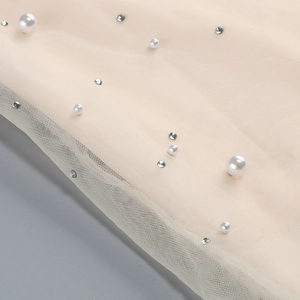 Detail of beaded mesh fabric with white pearls and crystals on a beige evening dress