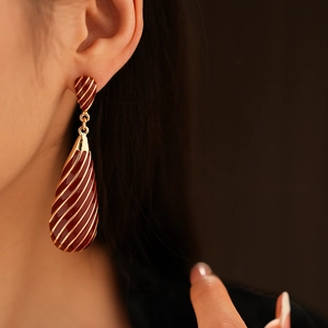 Gros plan de boucles d'oreilles vintage rouge foncé en émail avec des rayures dorées sur modèle