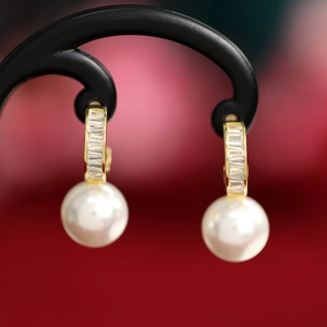 Macro detail of gold pearl earrings with baguette-cut crystals on a display stand