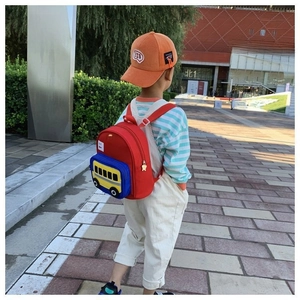 Outdoor back view of a child wearing a red cartoon school bus backpack with 3D pockets