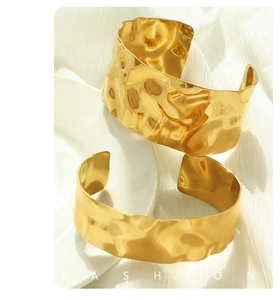 Detail of wide gold cuff bracelet featuring irregular hammered metal texture design