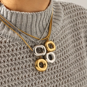 Détail de colliers superposés en or et argent avec pendentifs carrés et anneaux évidés