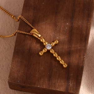 Detailed close-up of 18K gold-plated beaded cross pendant with a center zircon on wood