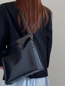 Minimalist black leather tote bag with adjustable strap and silver hardware on model