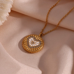 Détail macro d'un pendentif pièce dorée avec cœur en émail blanc et strass brillants