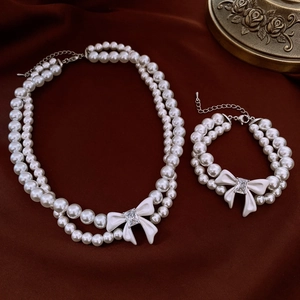 Close-up of double-layer pearl necklace and bracelet with crystal bow on red silk