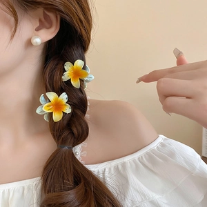 Detailed view of yellow gradient plumeria hair clips styled on braided hair
