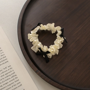 Dettaglio di scrunchie plissettato crema con piccoli fiocchi neri su vassoio in legno