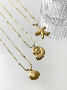 Detail of gold starfish and shell pendants on a beaded chain with a mirror reflection