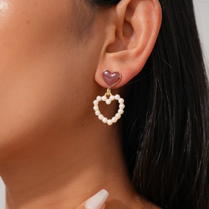 Elegant gold-framed red enamel and pearl heart drop earrings worn by a model