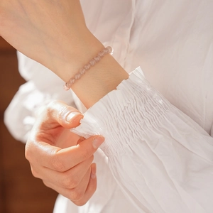 Close-up of strawberry quartz beaded bracelet on female wrist with elegant sleeve
