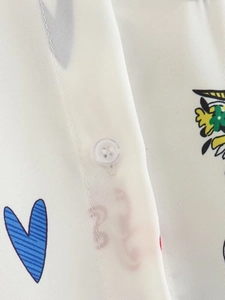 Détail du tissu blanc avec imprimé fleurs et cœurs bleus et bouton en résine