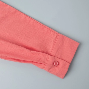 Detail of coral pink cotton shirt cuff showing natural fabric texture and button sewing