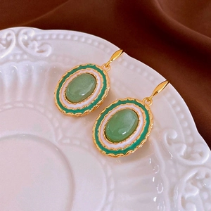 Close-up of vintage gold earrings with green gemstones and white enamel on a ceramic plate