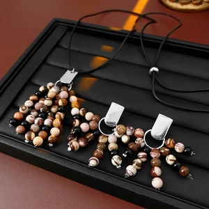 Close-up of vintage beaded fringe necklace with metallic accents on a black display tray