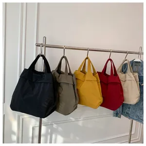 Multiple lightweight nylon tote bags in black, green, yellow, and beige hanging on a wall