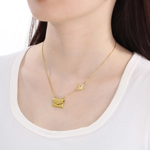 Gros plan du pendentif enveloppe dorée et breloque hirondelle sur collier acier