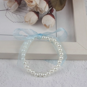 Close-up of children's white faux pearl bracelet with a blue satin ribbon bow detail