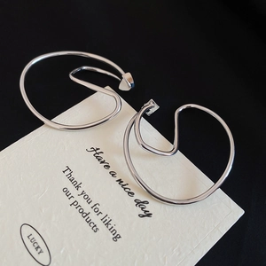 Detailed close-up of large irregular silver hoop earrings on a textured brand card
