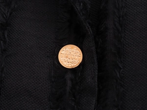 Detail of vintage golden button on textured black wool coat with embossed pattern